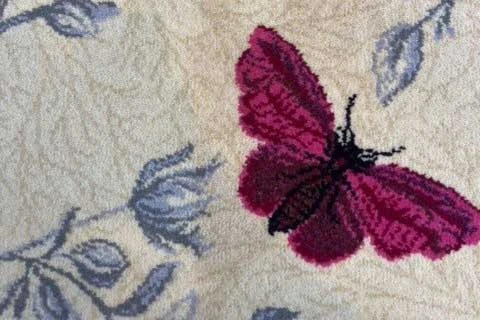 Close up of a patterned carpet with a butterfly and some flowers.