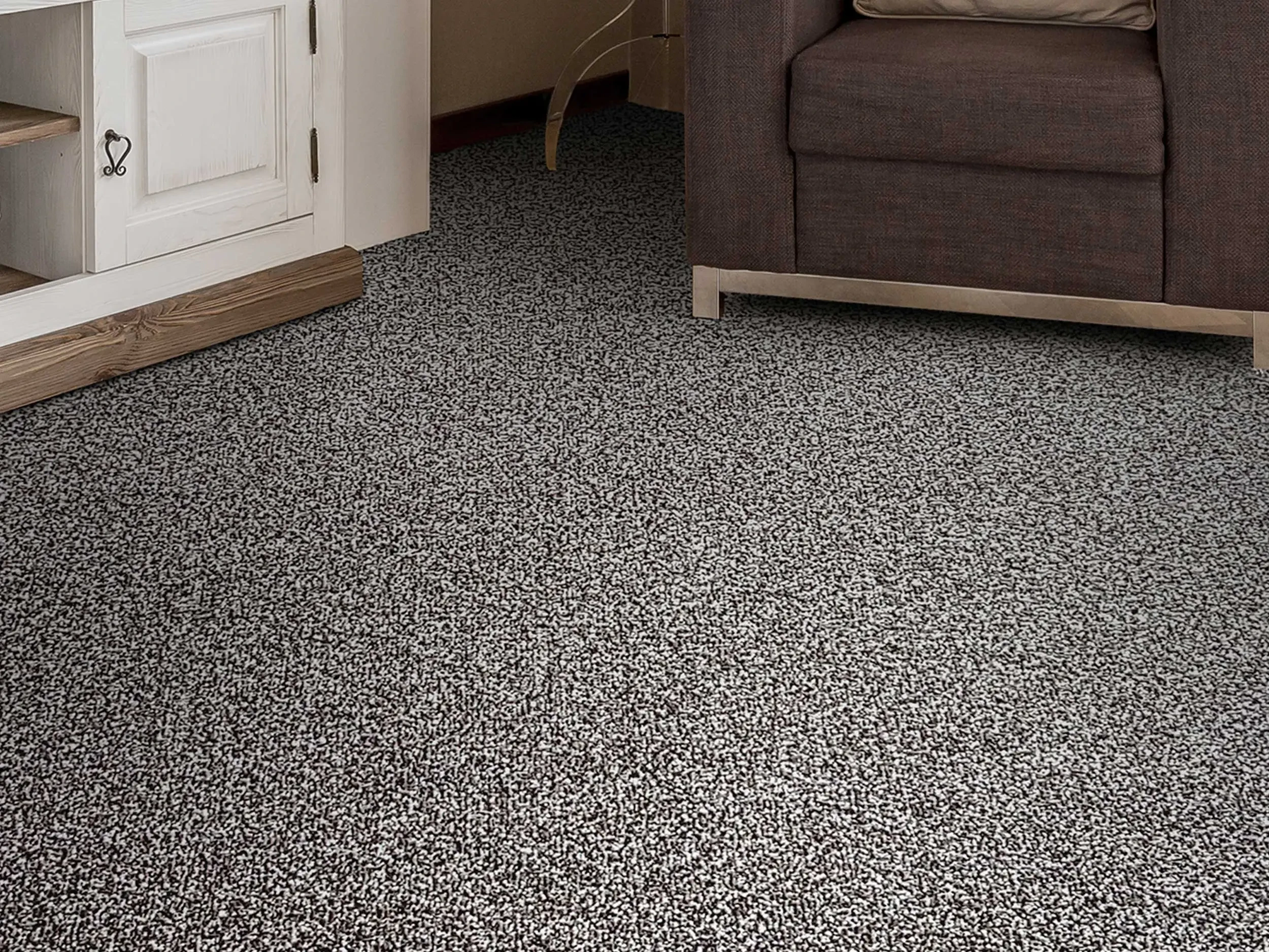 Close up of deep pile carpet in grey tone in a living room with a cabinet and chair in background.