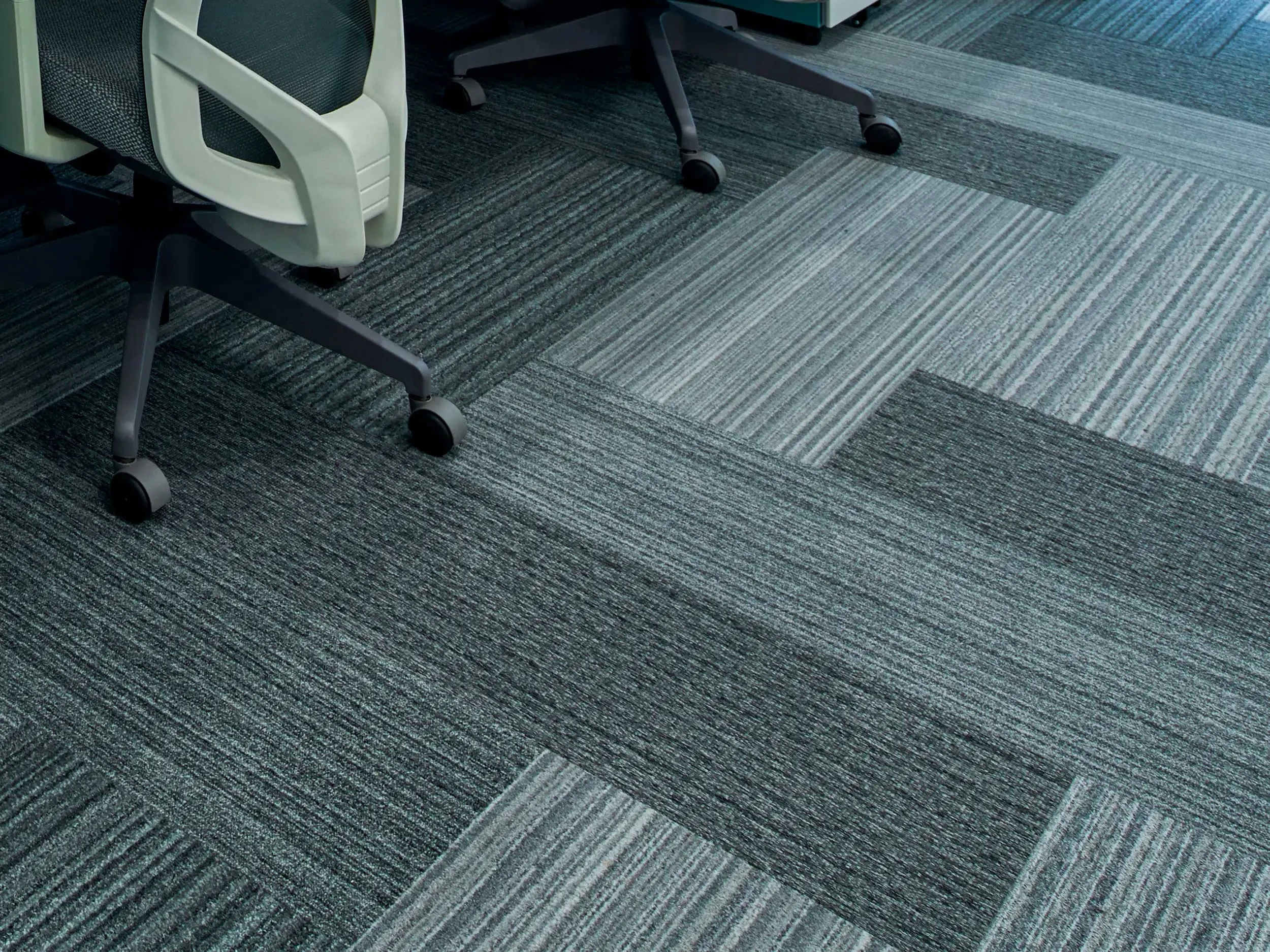 Close up of striped commercial carpet tile with office chair wheels in background.